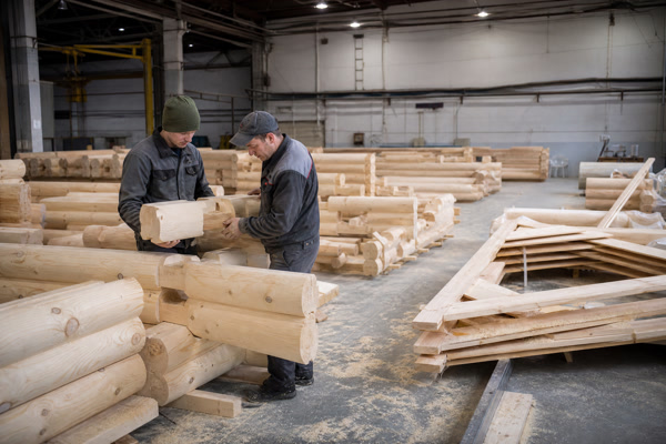 Factory workers checking pre-cut log cabin components and corner joints