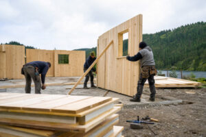 Crew assembling prefabricated timber wall panels on a cabin foundation